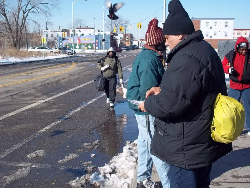 Neighbors carrying their belongings walk along a snowy Detroit street corner on a winter morning