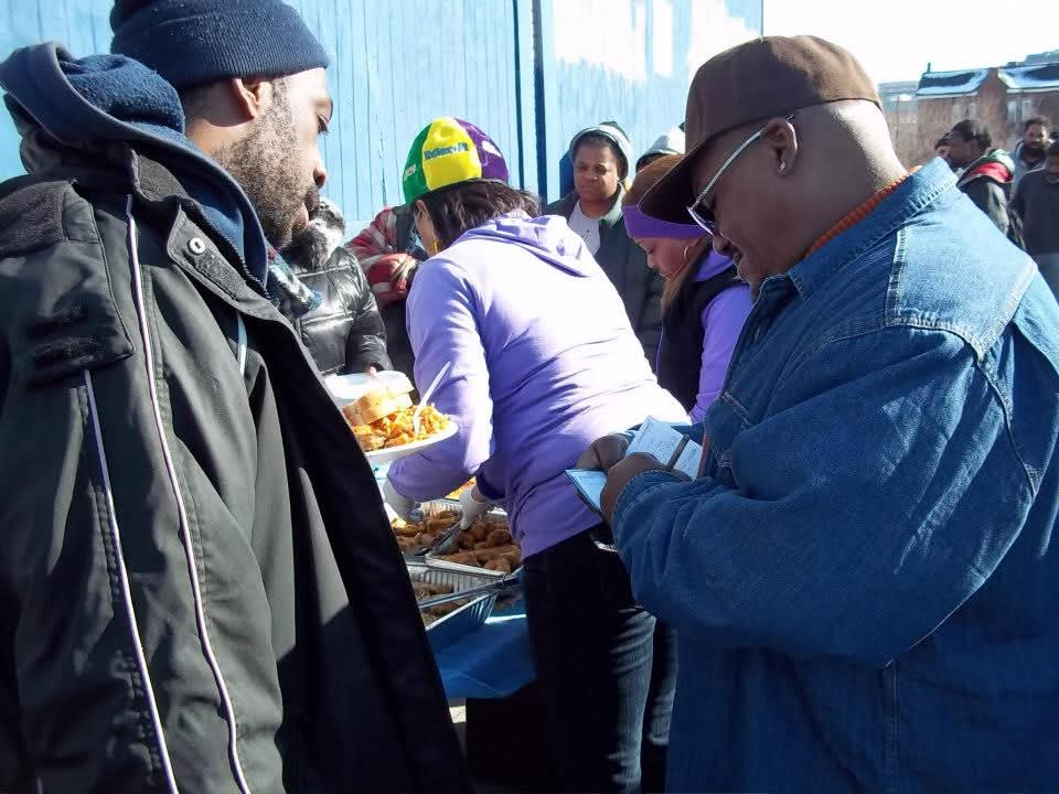 Neighbors receive plates of hot food from volunteers along a serving line in downtown Detroit